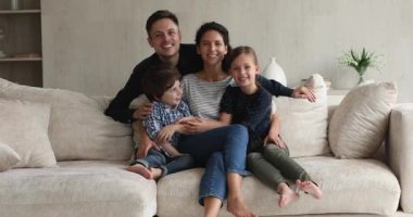 Çocuklu mutlu bir aile kanepeye oturur kamera karşısında poz verir.