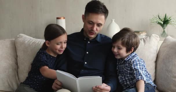 Vader zit op de bank met kinderen die sprookjesboek lezen. — Stockvideo