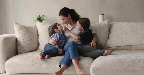 Любящая мама обнимает детей приятно болтать сидеть на удобном диване — стоковое видео