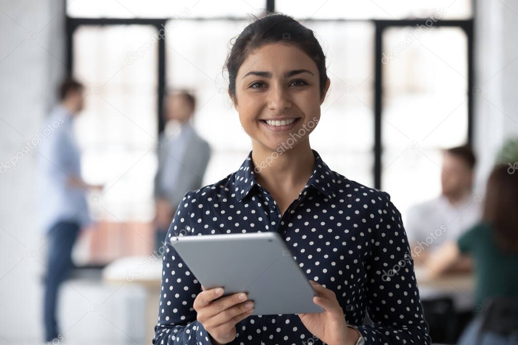 Portrait of happy Indian millennial employee using tablet in office