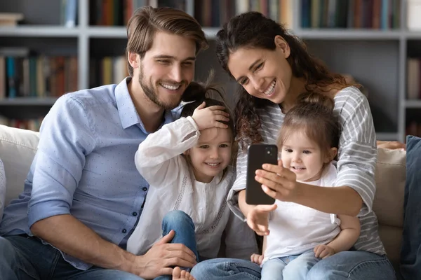 Lachende ouders en kleine dochters praten op smartphone — Stockfoto