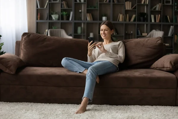Тисячолітня жінка відпочиває на дивані насолоджуйтесь онлайн знайомствами за допомогою телефону — стокове фото