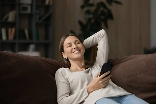 Millennial-Weibchen liegen auf Couch und genießen Song aus Handy-Playlist — Stockfoto