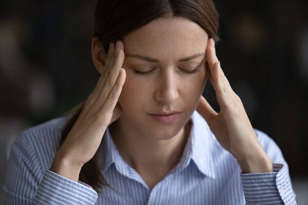 Молодая женщина с закрытыми глазами трогает виски, чувствуя мигрень.