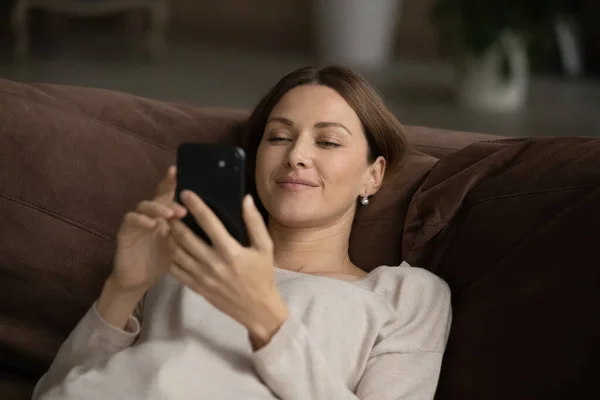 Счастливая молодая женщина лежит на диване просматривать веб-на смартфоне — стоковое фото