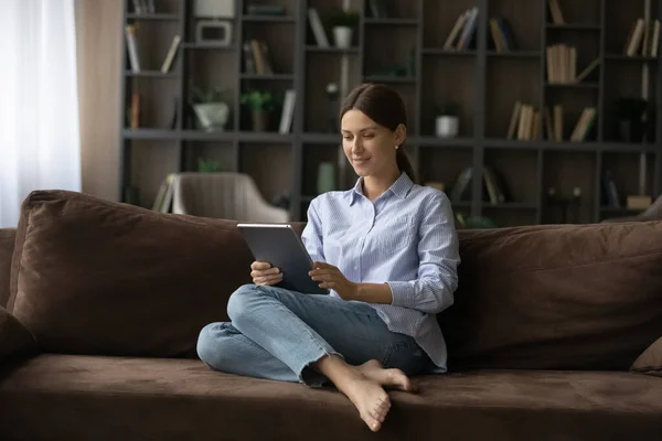 Jovem feliz descansar no sofá confortável segurando tablet digital — Fotografia de Stock