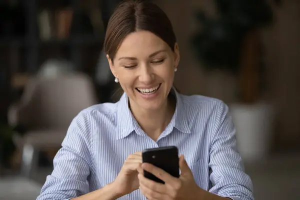 Mujer joven positiva disfrutar de la navegación web en el teléfono en la oficina — Foto de Stock
