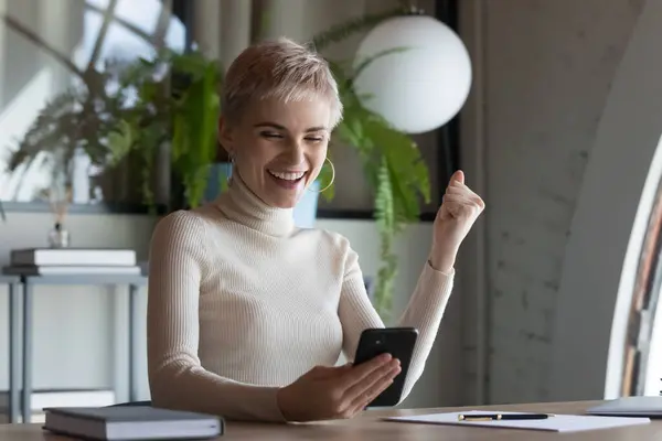 Excited female employee triumph with good news on smartphone — Stock Photo, Image