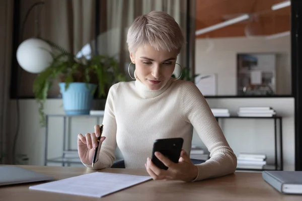 Successful female employee use smartphone working with paperwork — Stock Photo, Image