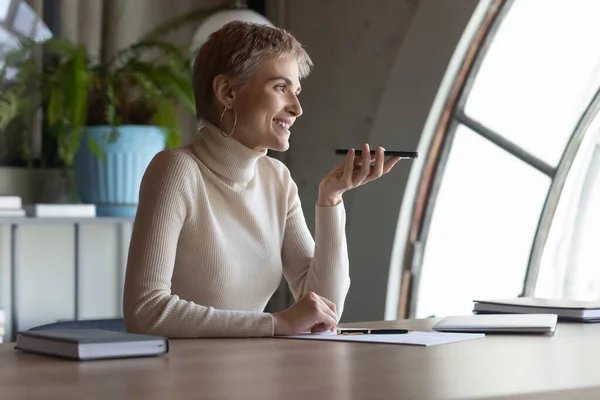 Smiling woman talk on loudspeaker on cellphone in office — Stock Photo, Image