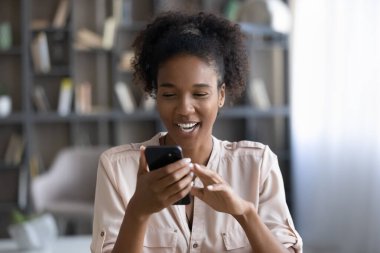Neşeli genç Afrikalı melez kadın telefon ekranına bakıyor..