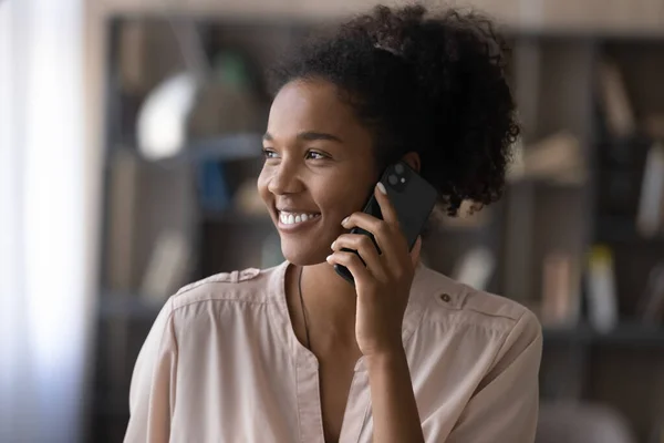 Smiling dreamy millennial african woman holding mobile phone call.
