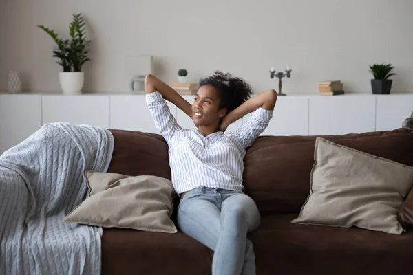 Relajada sonriente joven africana sentada en cómodo sofá. — Foto de Stock