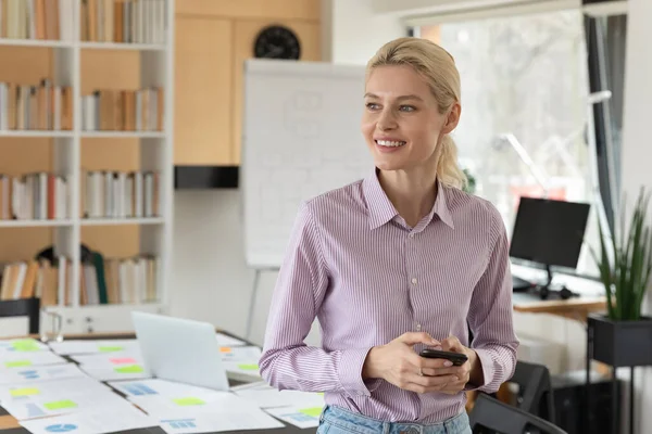 Close up dreamy smiling businesswoman holding smartphone, looking to aside — Stock Photo, Image