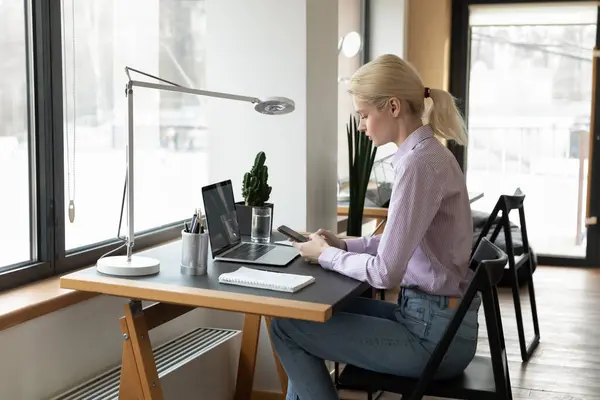 Fiduciosa donna d'affari che utilizza smartphone, seduta alla scrivania in ufficio — Foto Stock