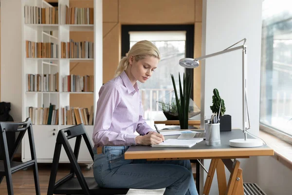 Seitenansicht selbstbewusste Geschäftsfrau macht sich Notizen, sitzt am Schreibtisch — Stockfoto