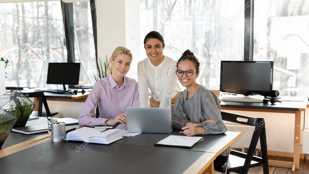 Portrait of three diverse businesswomen sitting at table in office