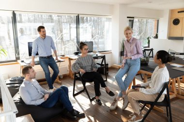 Çeşitli meslektaşlar brifinge katılıyor, daire içinde oturuyor, projeyi tartışıyorlar.