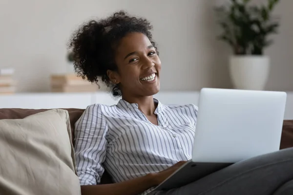 Portrait of sincere happy young african woman sitting on sofa with computer. — Stock Photo, Image