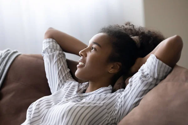 Drömmande ung afrikansk amerikansk kvinna avkopplande på bekväm soffa. — Stockfoto