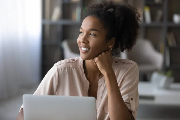 Glad vacker afrikansk kvinna drömmer, arbetar på dator. — Stockfoto