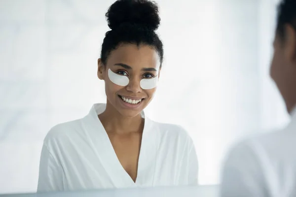 Glimlachende jonge zwarte vrouw met huidverzorging onder het oog collageen pleisters — Stockfoto