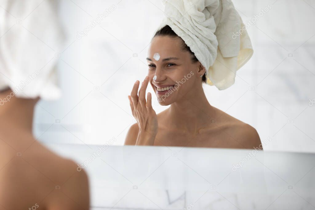Happy millennial girl enjoying home spa, applying cream