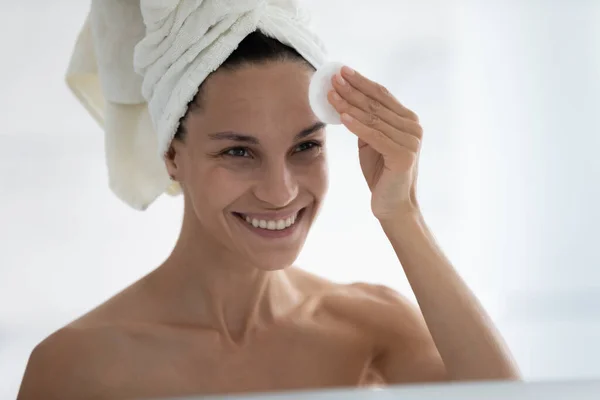 Happy beautiful millennial girl wrapped in towel cleaning facial skin — Stock Photo, Image