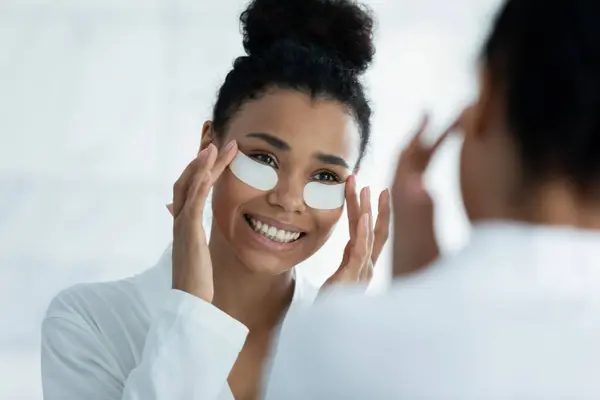 Feliz hermosa chica afroamericana aplicando almohadillas de colágeno hidrogel —  Fotos de Stock