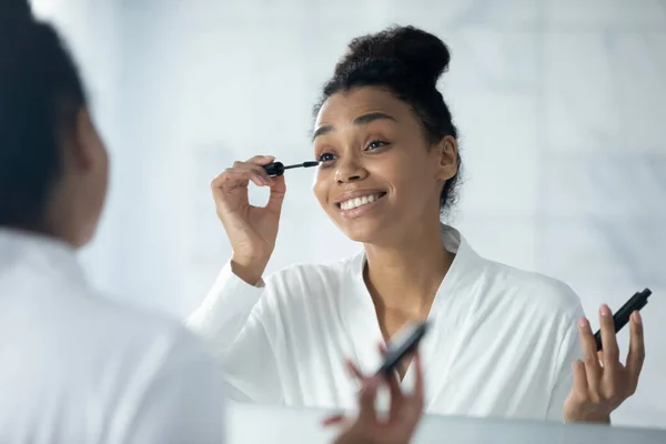 Glückliches Glamour-Millennial-Mädchen blickt in den Spiegel und trägt Wimperntusche auf — Stockfoto