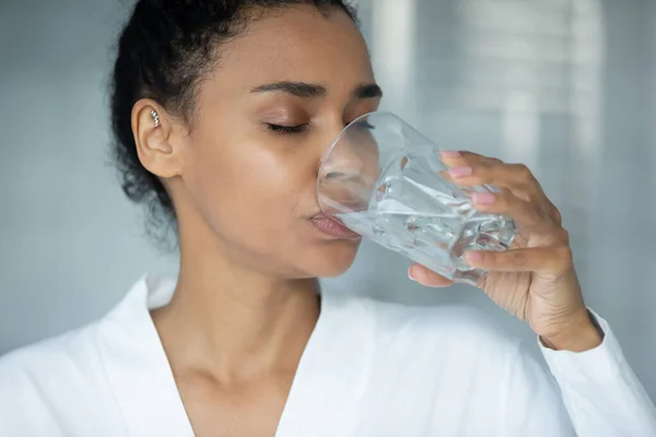 Мирная женщина смешанной расы в халате пьет воду хорошего качества — стоковое фото