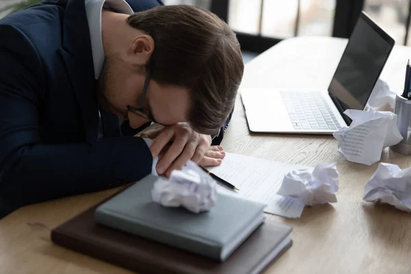 Уставший офисный работник отдыхает головой на рабочем столе с ноутбуком — стоковое фото