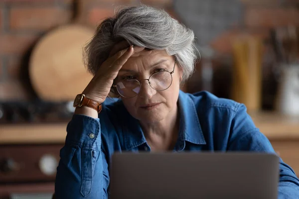 Зрелая женщина чувствует себя запутанным испытывает трудности с использованием ноутбука — стоковое фото