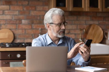Sakallı, olgun bir adam akıllı telefonuyla mutfakta oturuyor.