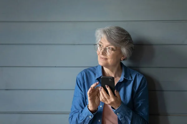 Older female holding smartphone posing in studio