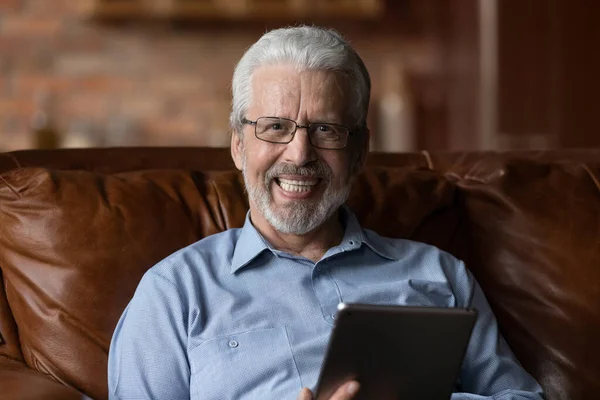 Homem mais velho relaxado sentar-se no sofá em casa com tablet — Fotografia de Stock