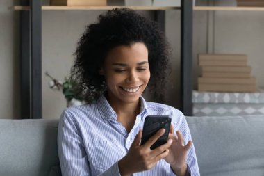 Gülümseyen Afrikalı Amerikalı kadın evde akıllı telefon kullanıyor.