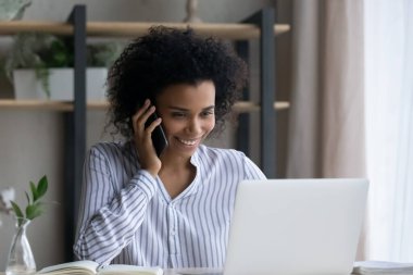 Gülümseyen melez kadın cep telefonunda dizüstü bilgisayarla konuşuyor.