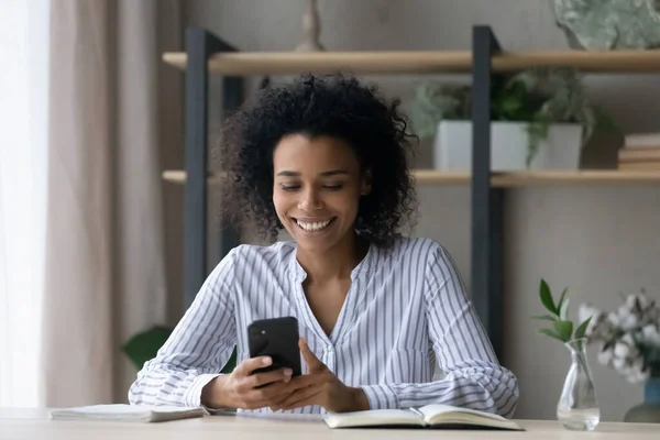 Femme afro-américaine souriante assis au bureau en utilisant un téléphone portable — Photo