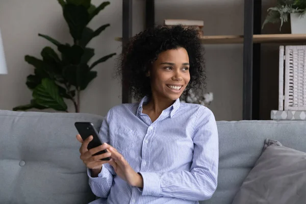 Sorridente donna afro-americana utilizzare il cellulare sognando — Foto Stock