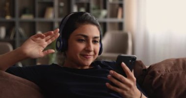 Hintli kadın kanepeye uzanıp kablosuz kulaklıkla müzik dinliyor.
