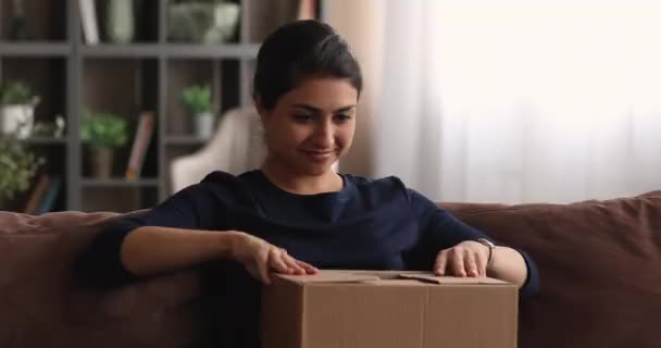 Young Indian woman sit on sofa opening parcel box — Stock Video