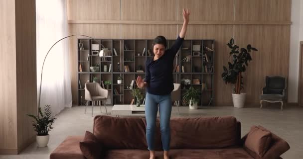 Indiska kvinna dansar hoppa barfota på soffan i vardagsrummet — Stockvideo