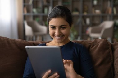 Pozitif Hintli kadın evinde tablet kullanarak kanepede oturuyor.