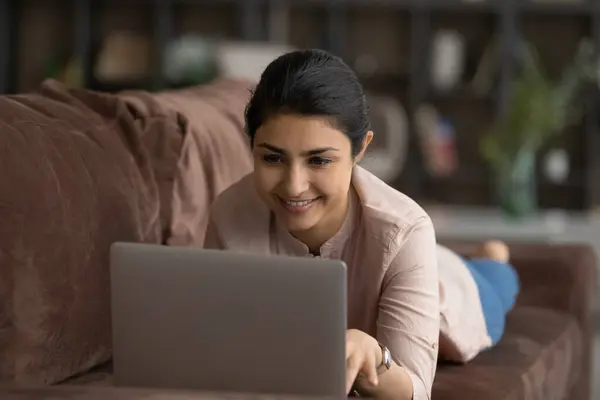 Teen indian female lie on belly on couch use laptop — Stock Photo, Image