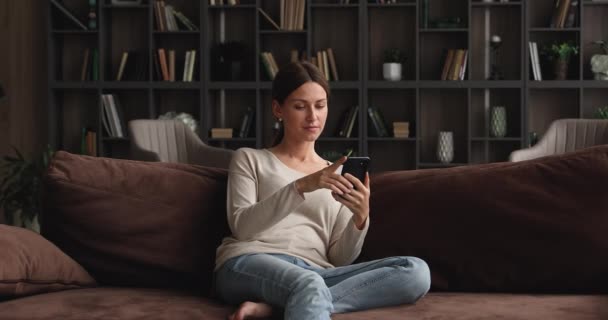 Belle femme relaxante sur canapé à la maison avec téléphone intelligent — Video