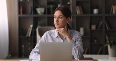 Ciddi bir kadın iş yerinde oturup laptopla çalışıyor, evrakları kontrol ediyor.