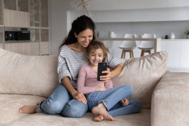 Gülümseyen Latin anne ve genç kız cep telefonu kullanıyor.