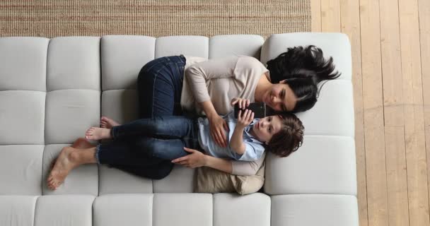 Por encima de la vista mamá e hijo acostados en el sofá con teléfono inteligente — Vídeo de stock