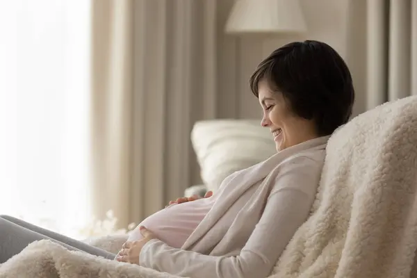 Vista laterale sorridente incinta giovane donna che tocca la pancia, in attesa di bambino — Foto Stock